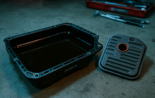 Aisin EAT8 automatic gearbox oil drain pan filled with dark degraded ATF fluid beside a used transmission filter