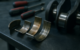 worn connecting rod bearing shells from a BMW S54 engine laid on a workbench beside a crankshaft journal